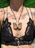 Person wearing a black lace top with a butterfly pendant necklace.