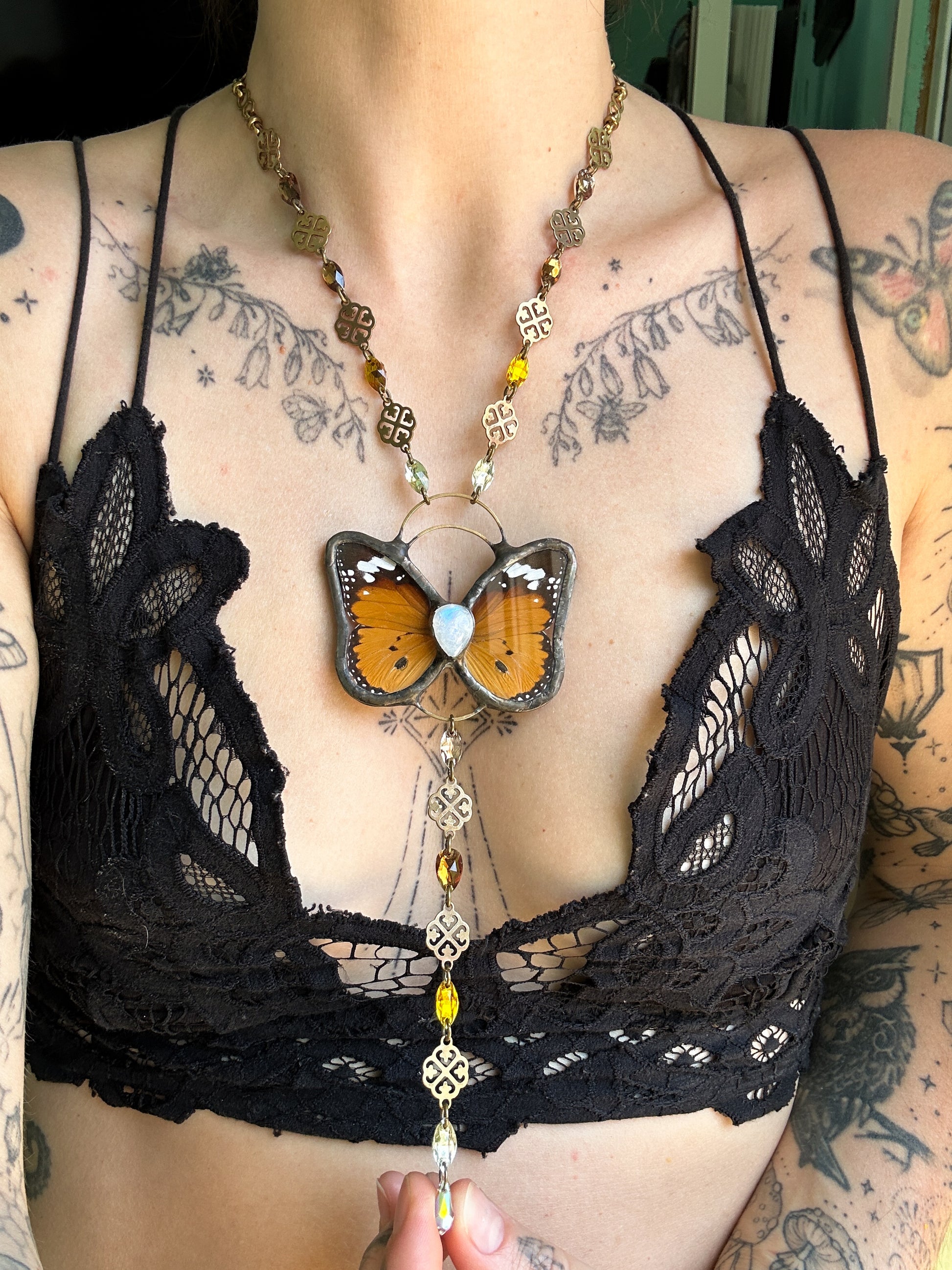 Black lace bra with a butterfly pendant necklace on a tattooed chest.