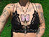 Person wearing a black lace top with a butterfly pendant against a grass background