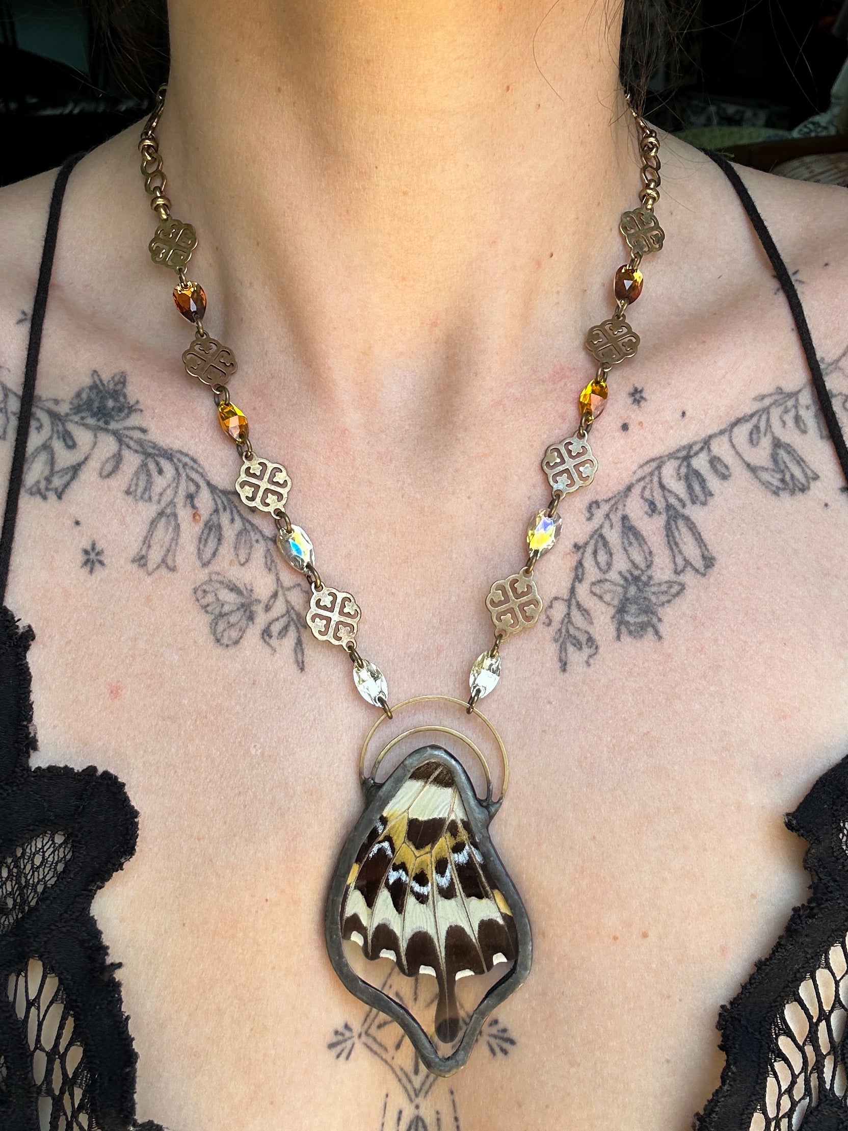 Necklace with butterfly pendant worn by a person with tattoos on their chest.