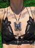 Person wearing a black lace top with a decorative butterfly necklace against a green grass background
